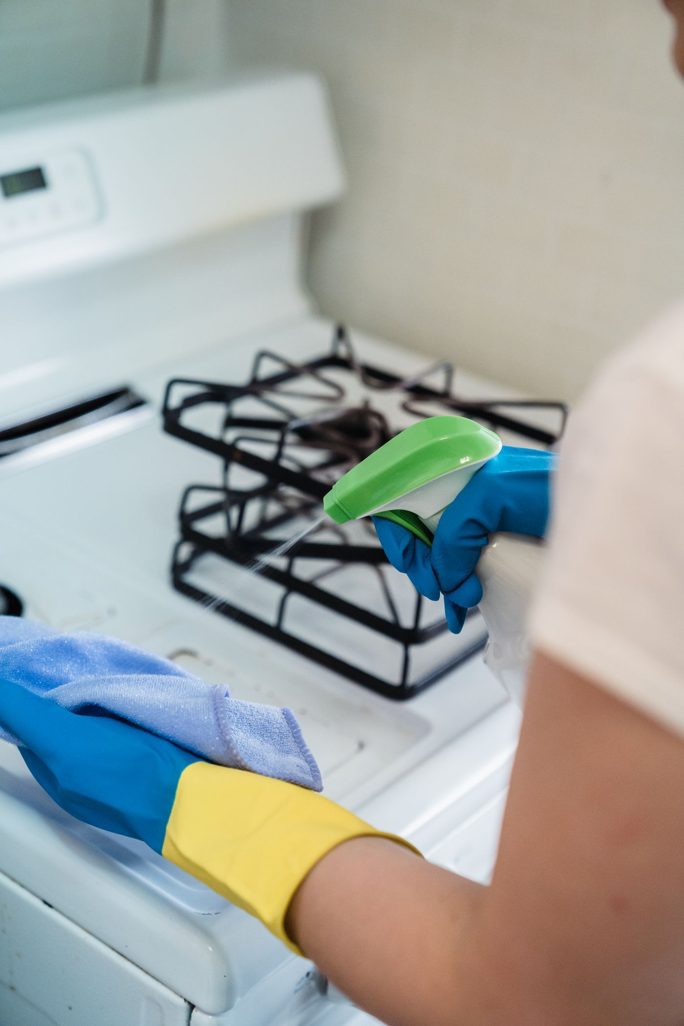Gloved hands scrubbing a kitchen stovetop during a deep cleaning